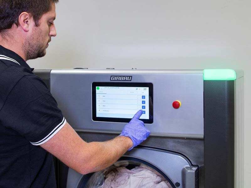 Technician selecting a cycle on a Girbau washer touchscreen in an on-premise laundry