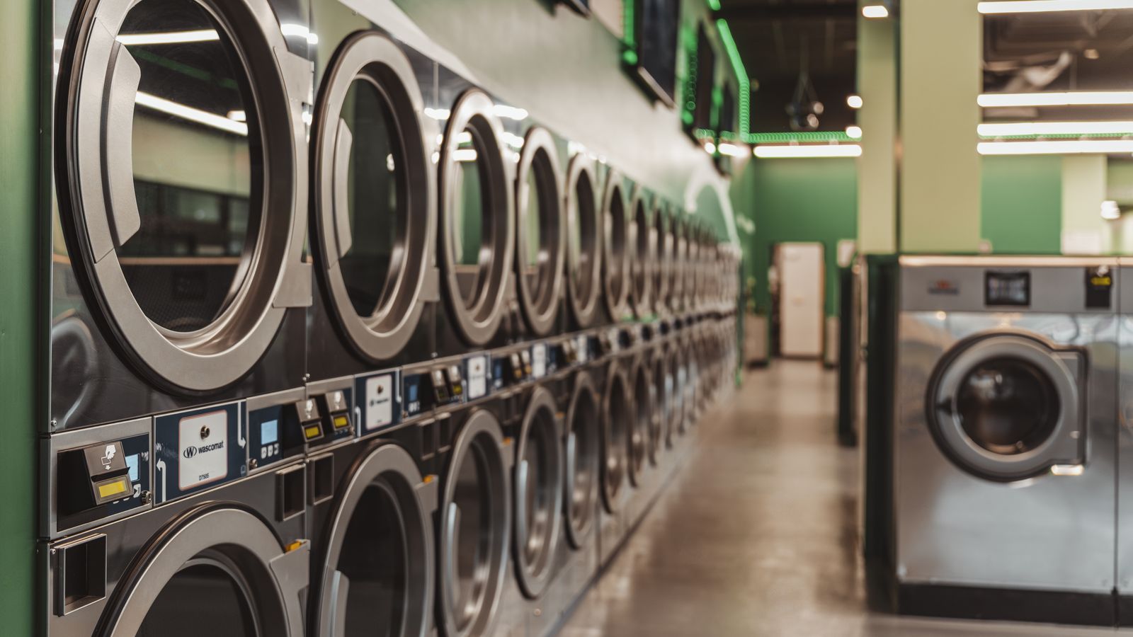 Interior of a modern self-service laundromat with a row of stacked commercial dryers and washers