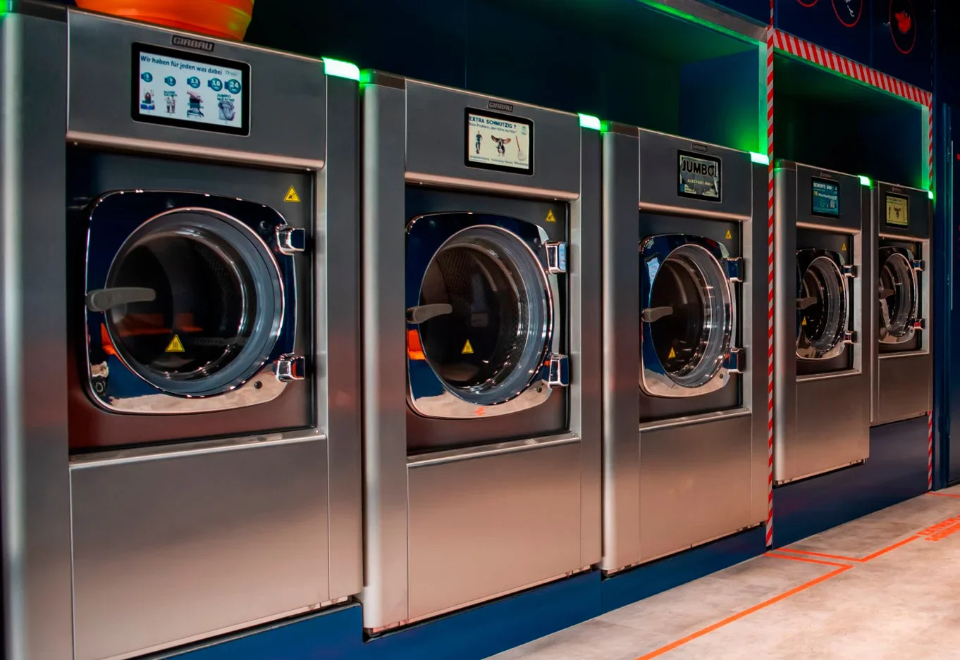 A row of Girbau commercial washers in a laundromat with their control screens lit