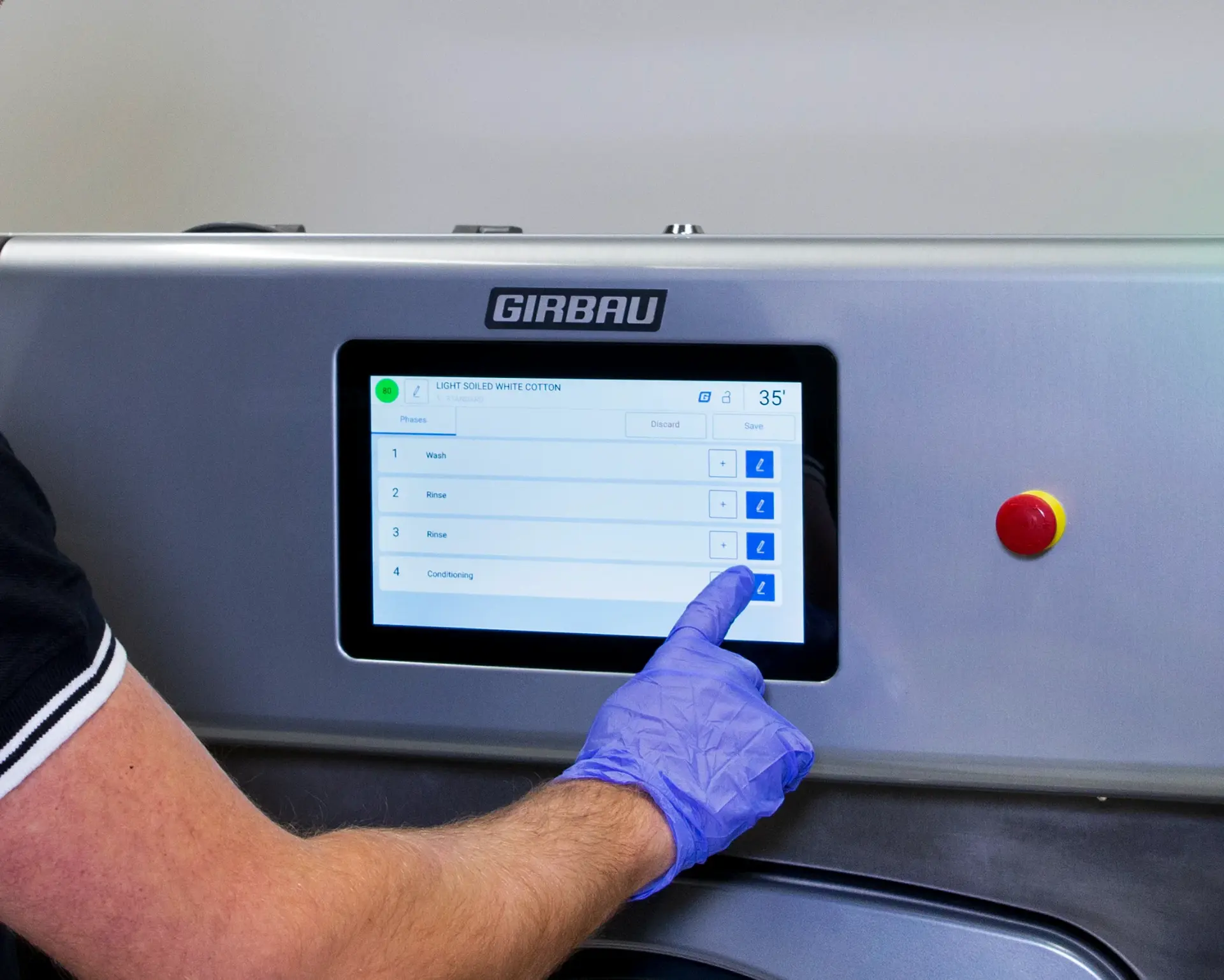A gloved hand selecting a wash cycle on the touchscreen of a Girbau commercial washer
