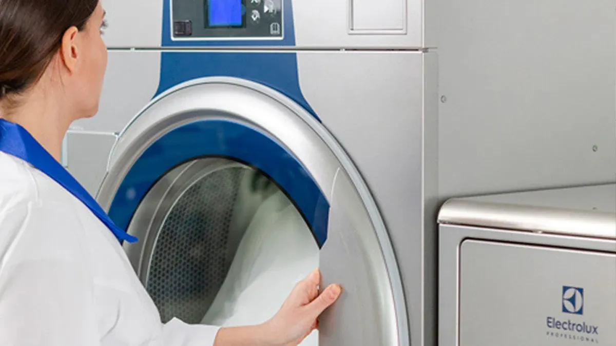 Laundry worker loading a stainless steel commercial tumble dryer