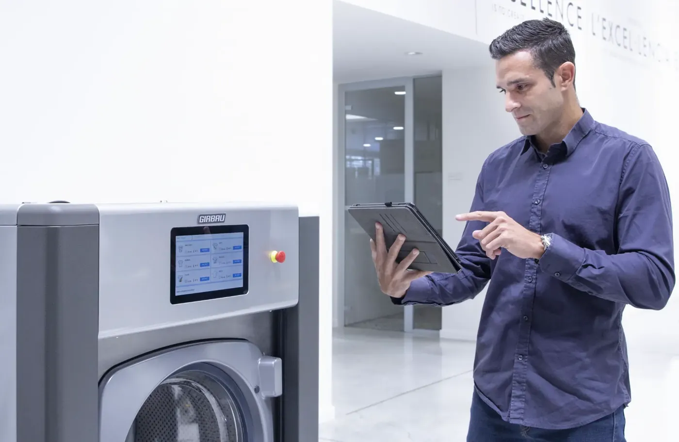 Technician operating a Girbau touchscreen while using a tablet to manage laundry programs