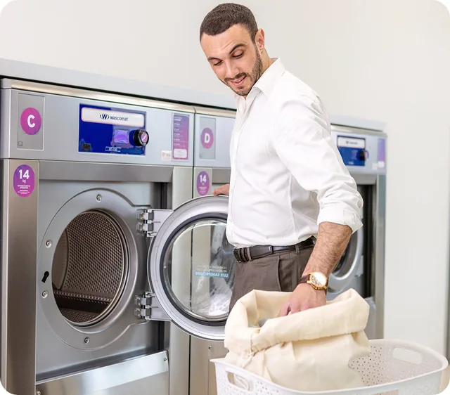 Staff member loading a Wascomat commercial washer in a laundromat